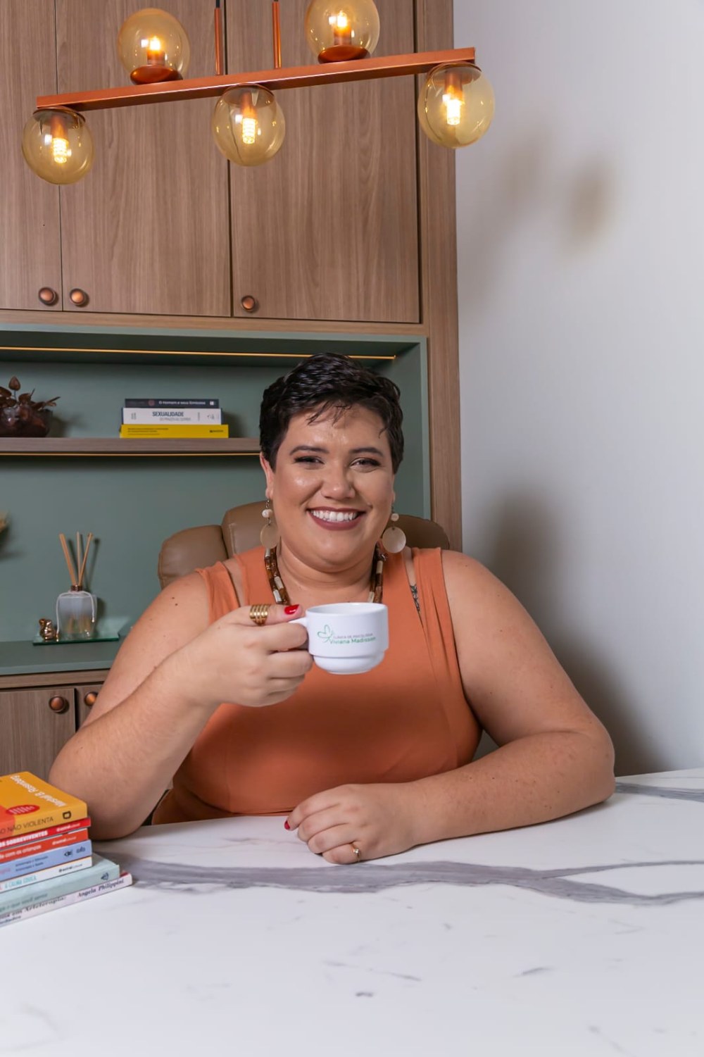 Laís Renata sorrindo, com uma xícara na mão, no consultório